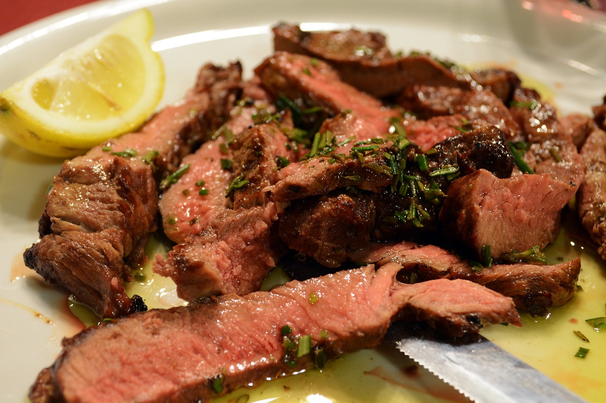 Plate of sliced beef or tagliata di manzo with rosemary and a lemon wedge