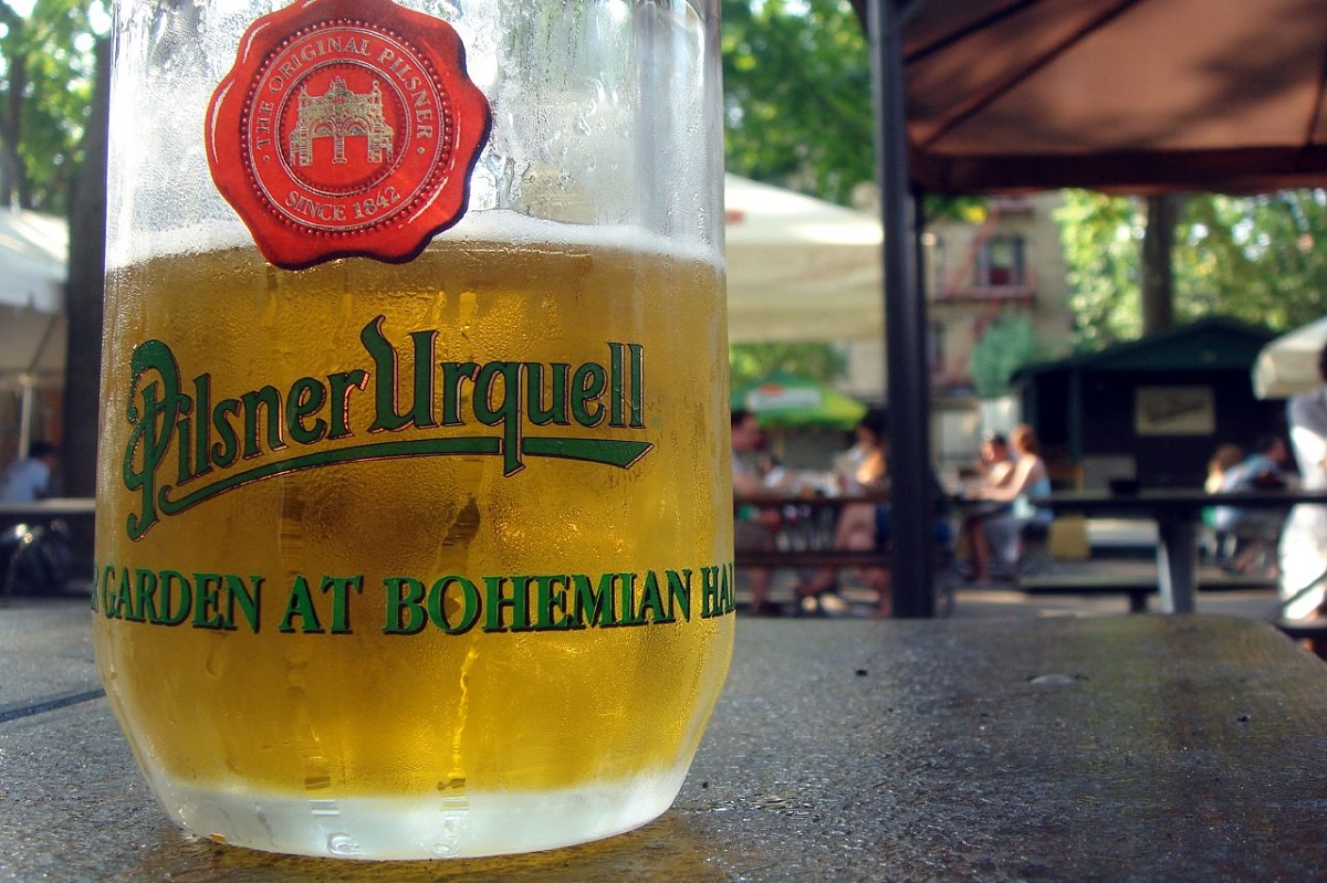 A close-up of a frosty, pale mug of beer at an outdoor terrace eating area