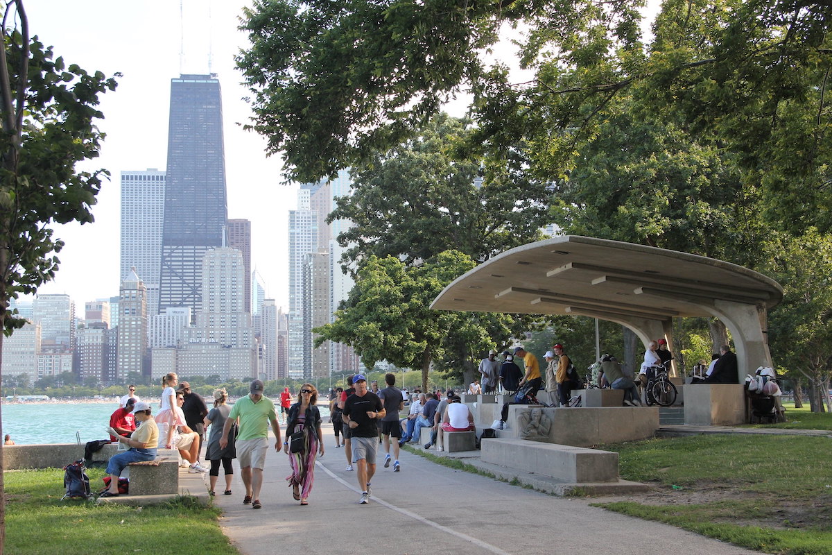 People are jogging, riding bikes, and sitting and hanging out on the Lakefront Trail in Chicago with the skyline in the background