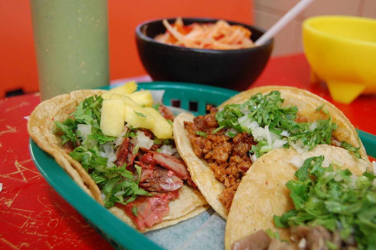 close up of three tacos in a green plastic basket on a red painted table
