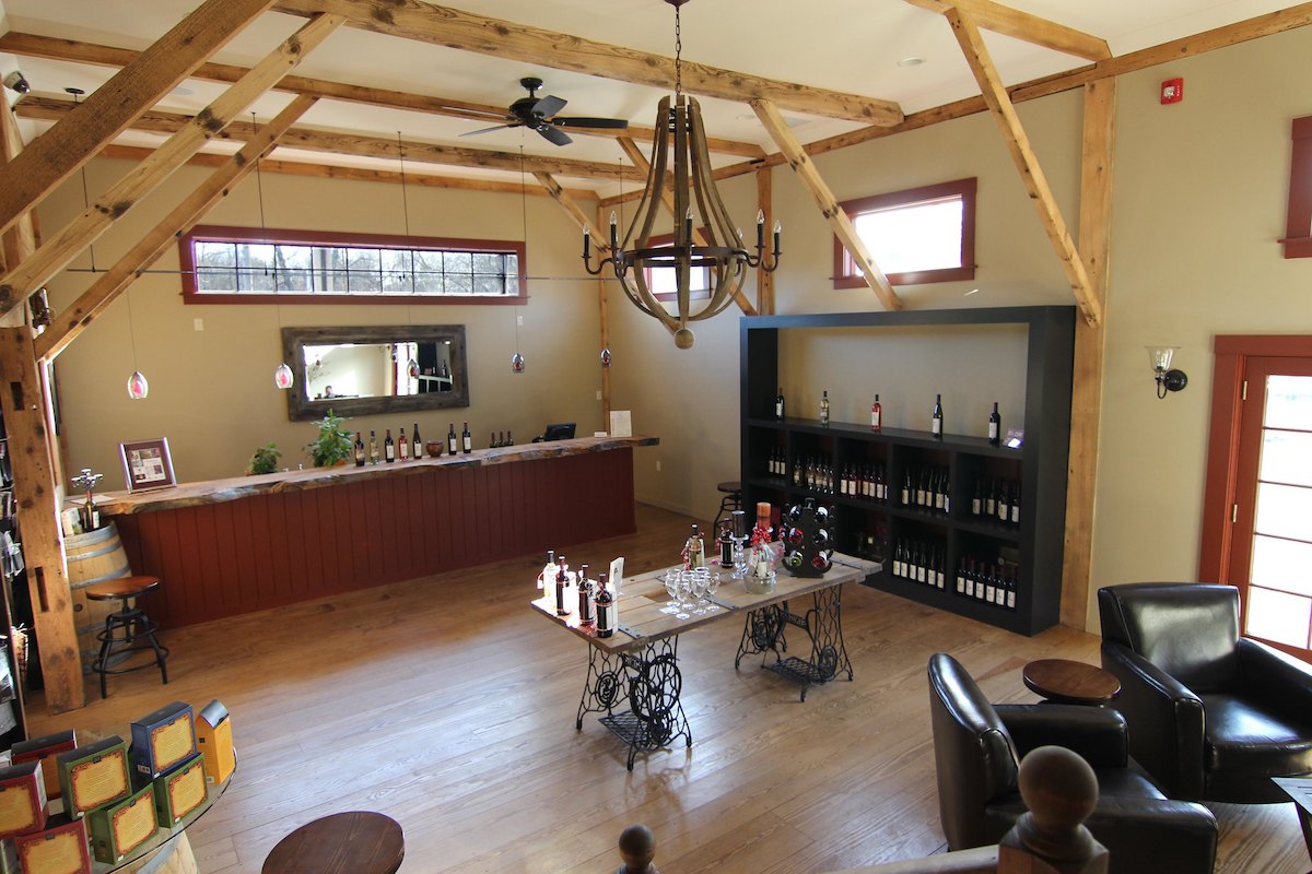 Wide angle shot of a winery tasting room in massachusetts with a long bar covered in wine bottles, a table in the middle of the room with wine glasses and wine bottles for tasting