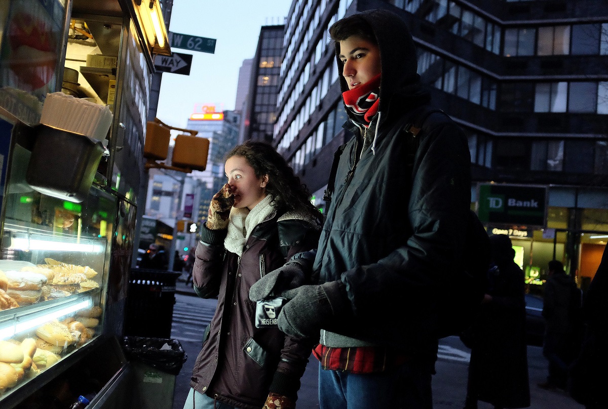 Two young people wearing coats pick out snacks at a food truck in new york at night