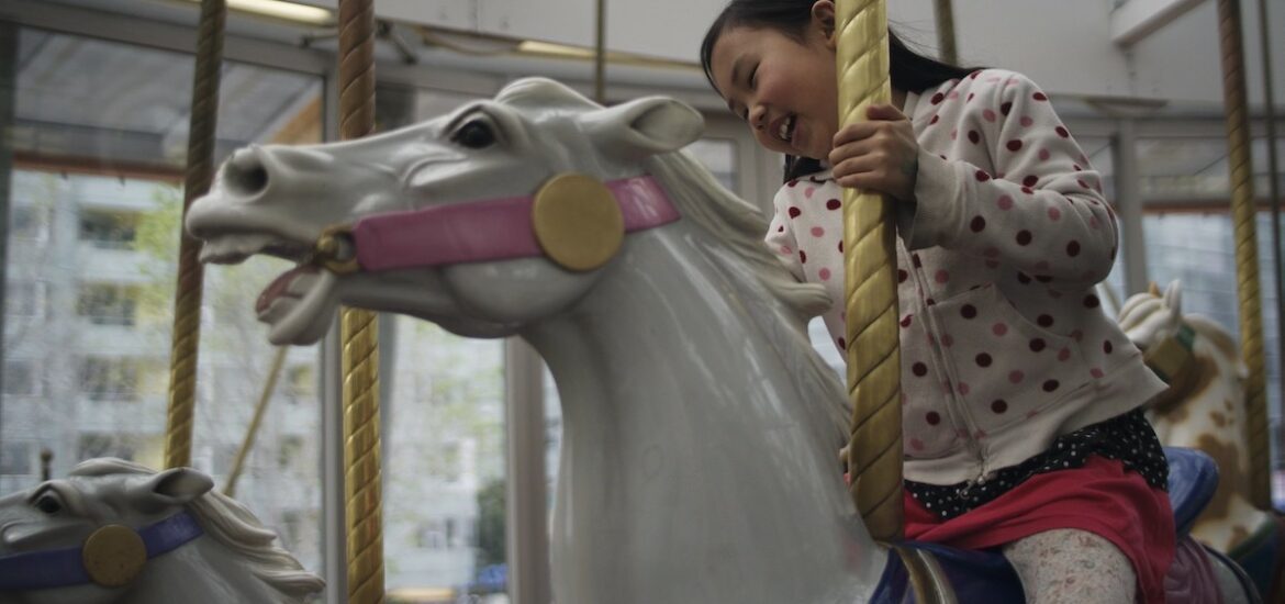 A girl smiles as she rides around on a white carousel horse
