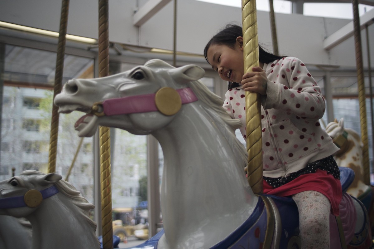 A girl smiles as she rides around on a white carousel horse