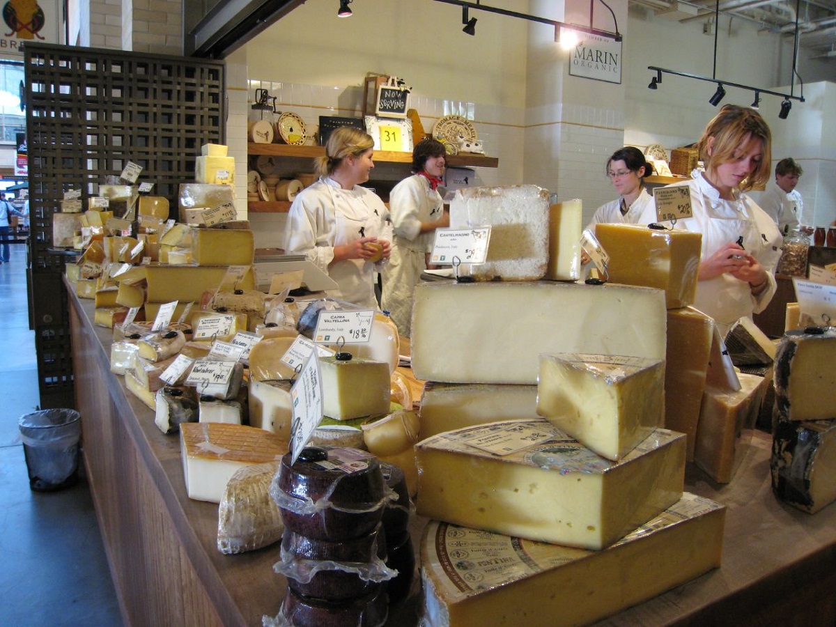 Stacks of cheese at the counter of a cheese shop with employees behind them in a San Francisco store