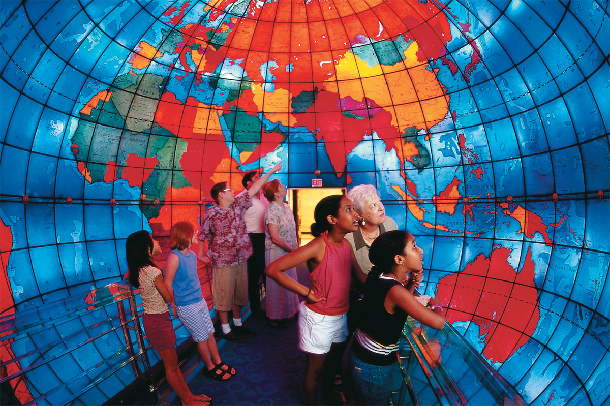 A group of people of varying ages in a dome-shaped room with the walls decorated with a colorful map of the world. The Mapparium is a true Boston hidden gem.