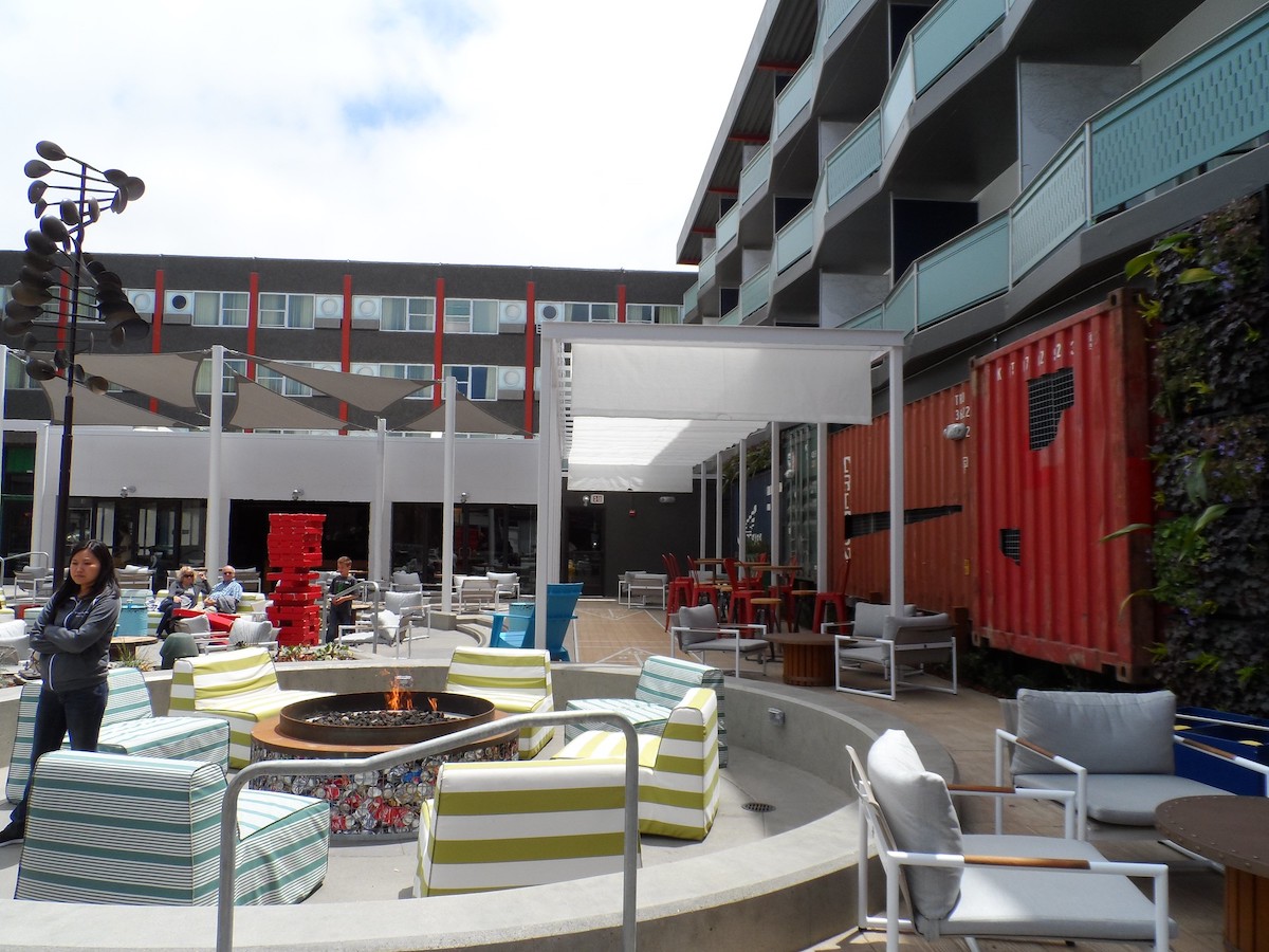 An outdoor courtyard of a modern building made of colorful shipping containers. There are firepits with circular couches surrounding them.