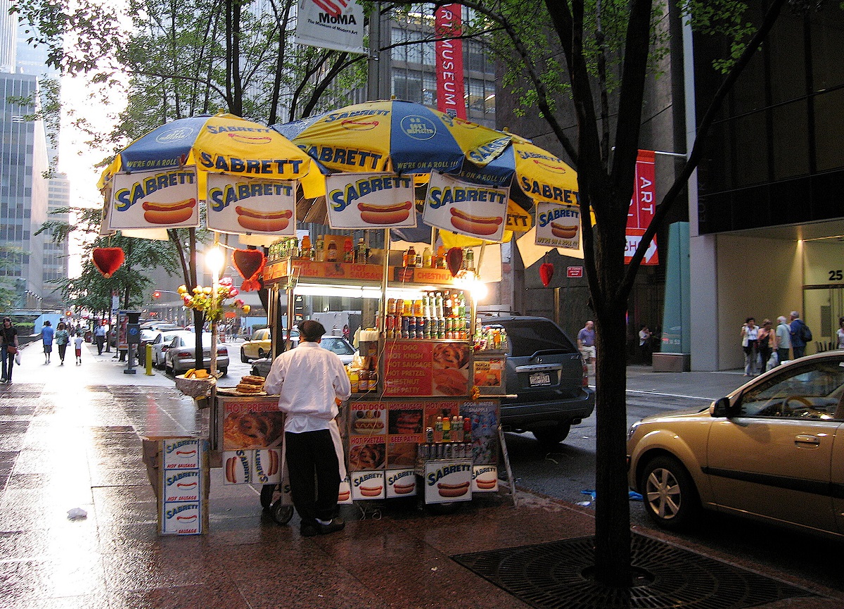 A hot dog stand with vendor on a rainy day