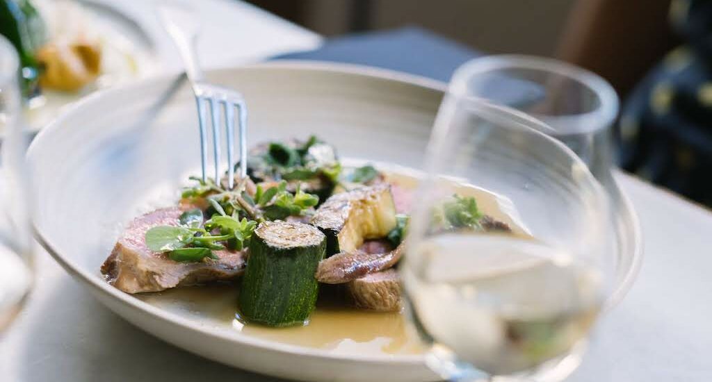 White wine and a fancy plate of food with zucchini and meat in Paris
