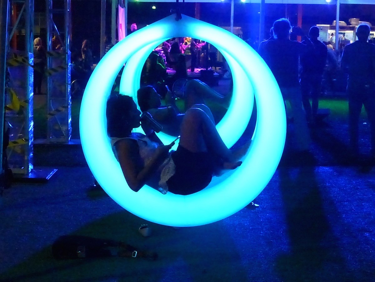 At night a woman sits in a hoop swing that is lit up blue