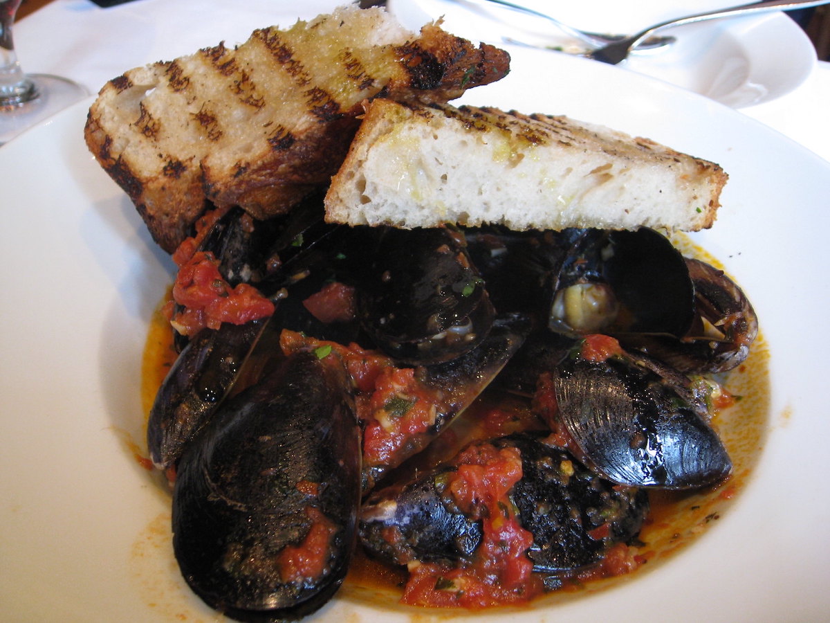 Close up of a bowl of stewed mussels with a tomato-based sauce and warm bread on top