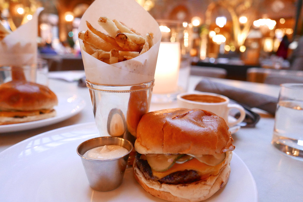 close up of a gourmet hamburger and fries with the beautiful courtyard of 3 Arts Cafe of Chicago in the background