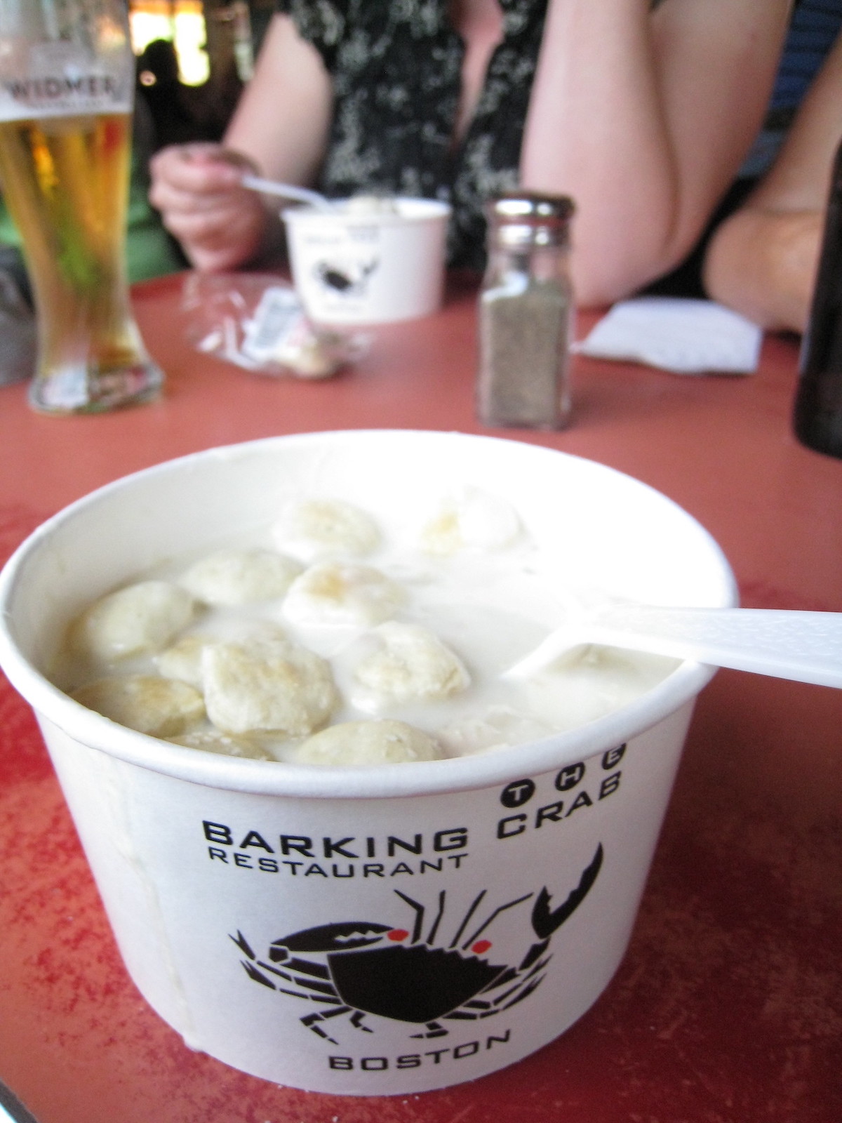 Close up of a paper cup filled with clam chowder and topped with oyster crackers