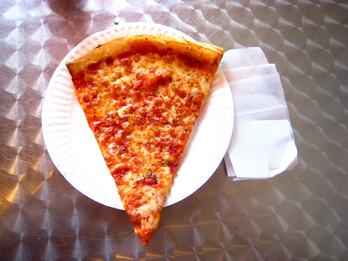 A slice of cheese pizza on a white paper plate is peak street food in Boston.