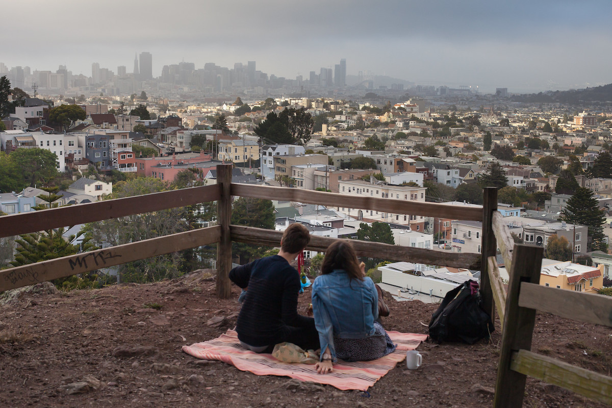 a couple sits on a pink blanket enjoying a picnic overlooking San Francisco