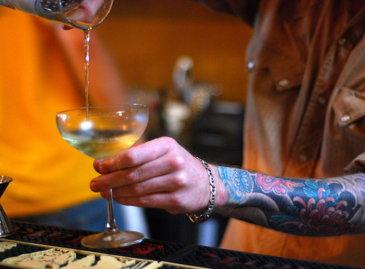 Close up of a bartender pouring a cocktail from a shaker into a coupe class