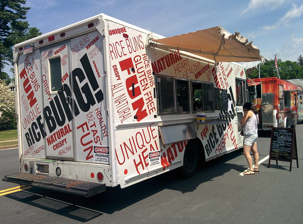A white food truck covered in black and red lettering. The truck is Riceburg, a popular on in Boston.