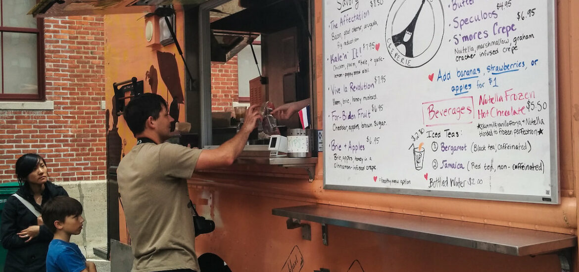 A man pays for his food through the window of an orange food truck