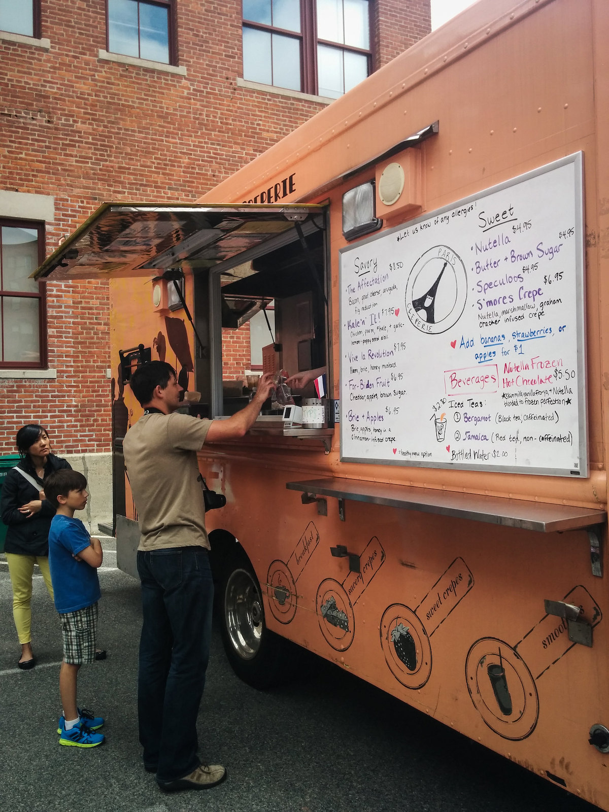 A man pays for his food through the window of an orange food truck