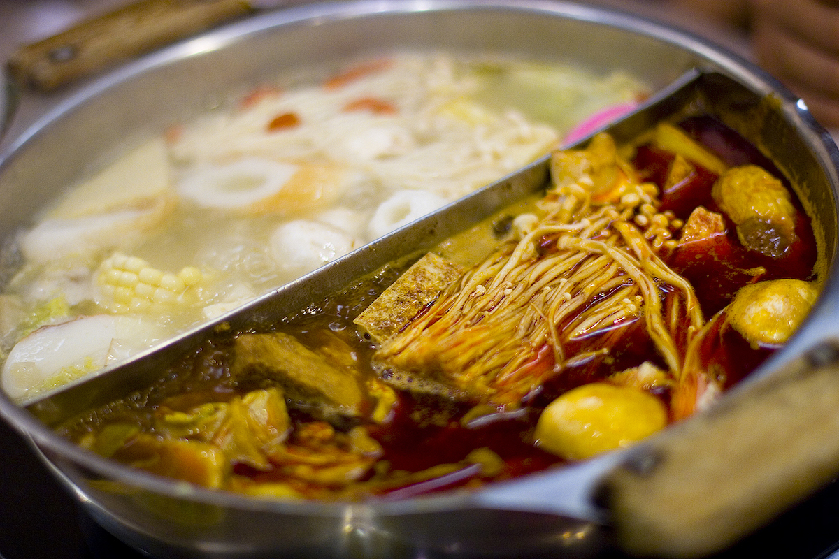 close up of a Chinese hot pot divided in half with a piece of metal, filled with two kinds of broth, half which is red and spicy, the other half is clear