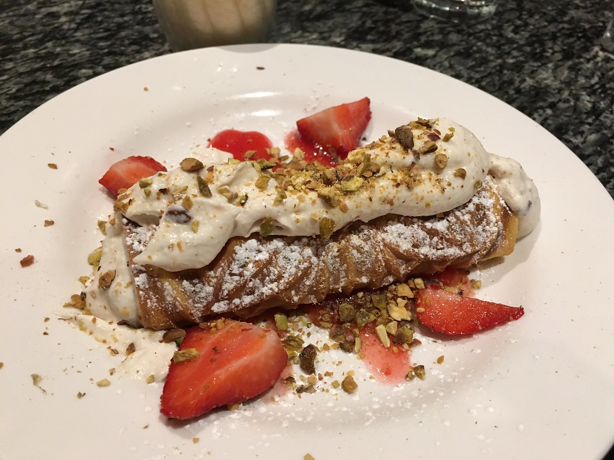 A white plate of cannoli with cream and strawberries