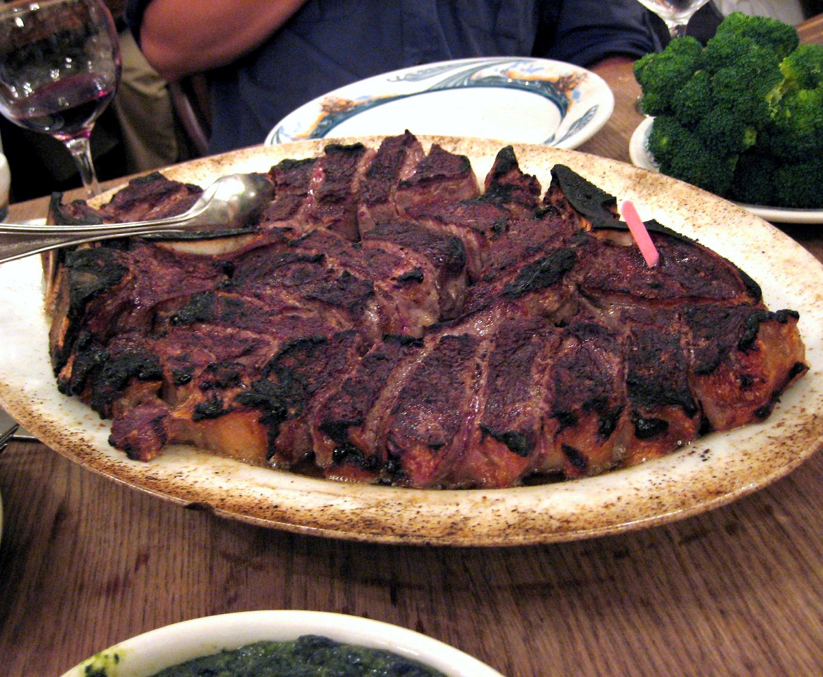 A huge plate of grilled and charred meat in a bowl on a wooden table