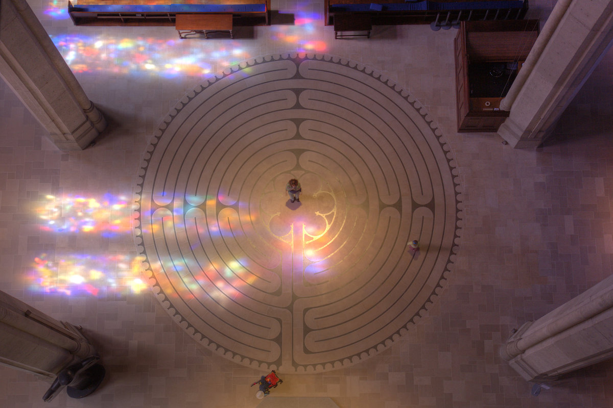 Overhead shot of someone standing in the interior Grace Cathedral Labyrinth, colorful refracted light from the stained glass spills across the floor