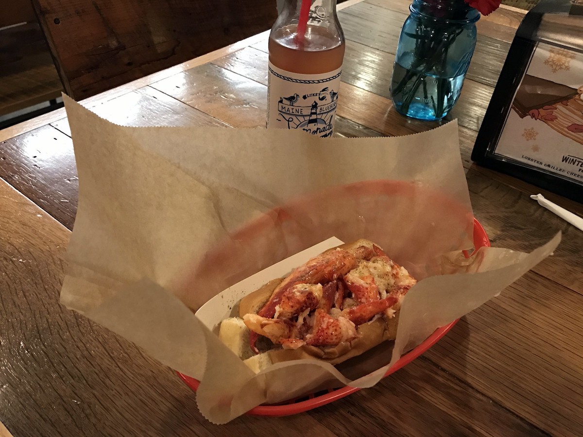 A lobster roll sits on a piece of parchment paper in a red plastic basket at Luke's Lobster in Boston 