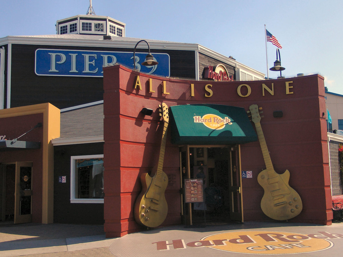 Photo of the entrance to the Hard Rock Cafe restaurant in San Francisco pier 39. Two golden guitars frame the doorway on a red building with a green awning