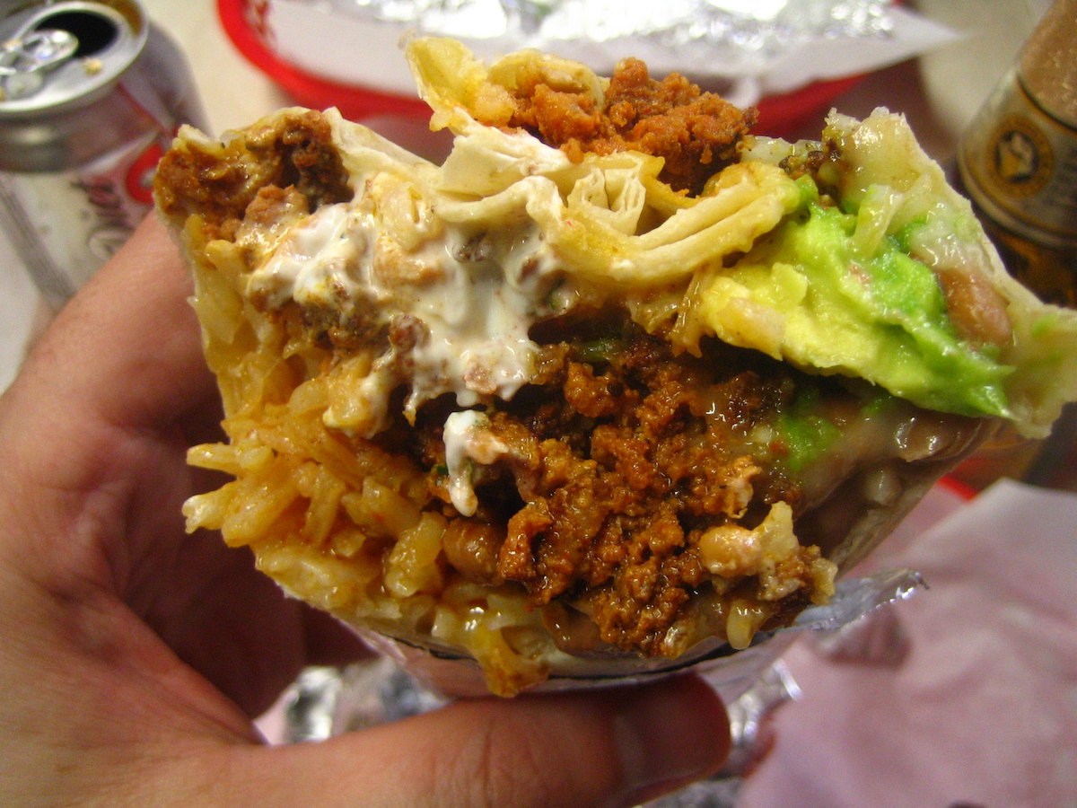 Close up of a cross-section of a Mission-style burrito, a food San Francisco is known for. The burrito is filled with rice, chorizo, sour cream, and guacamole.