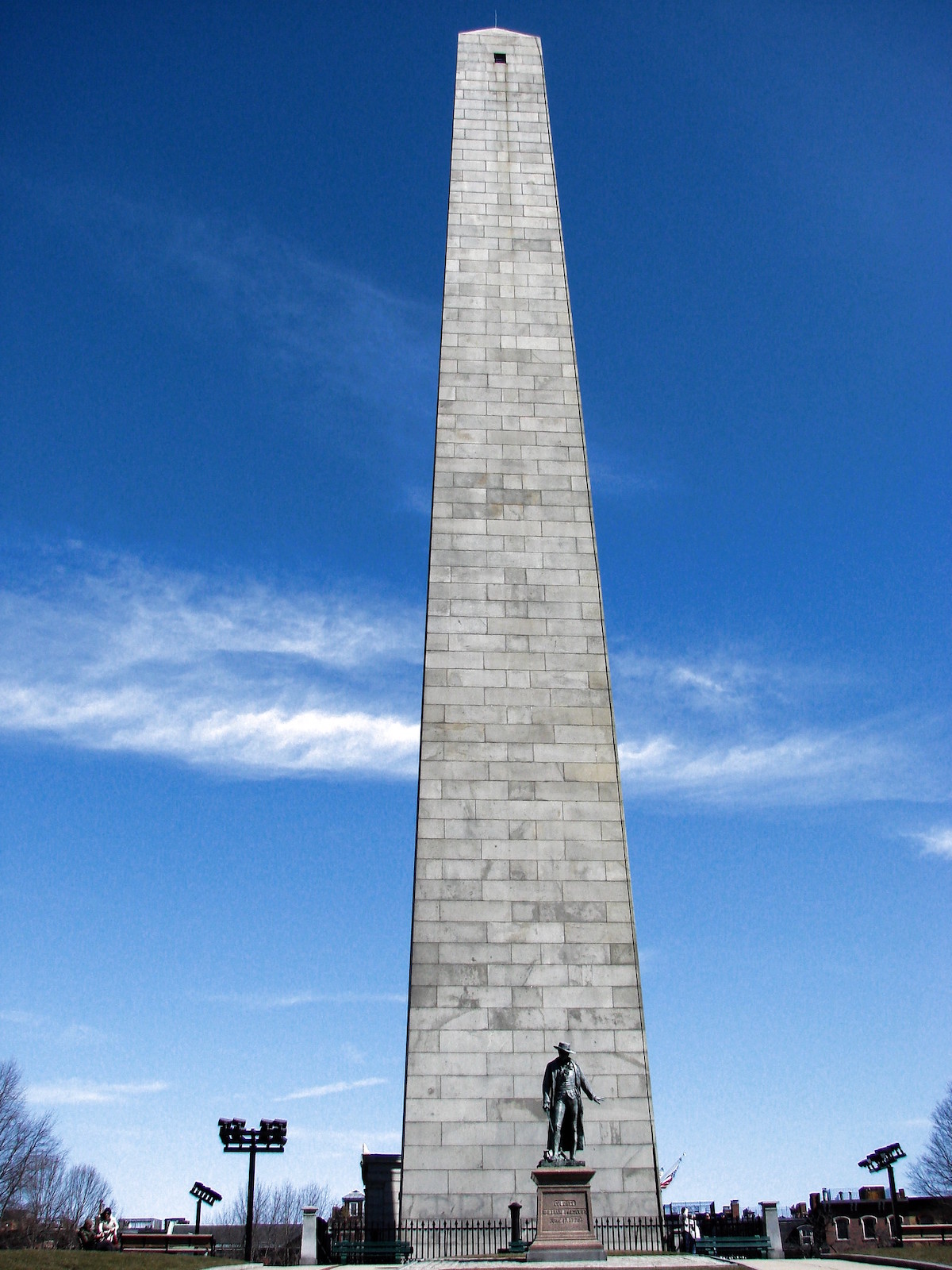 tall grey obelisk looms over a statue