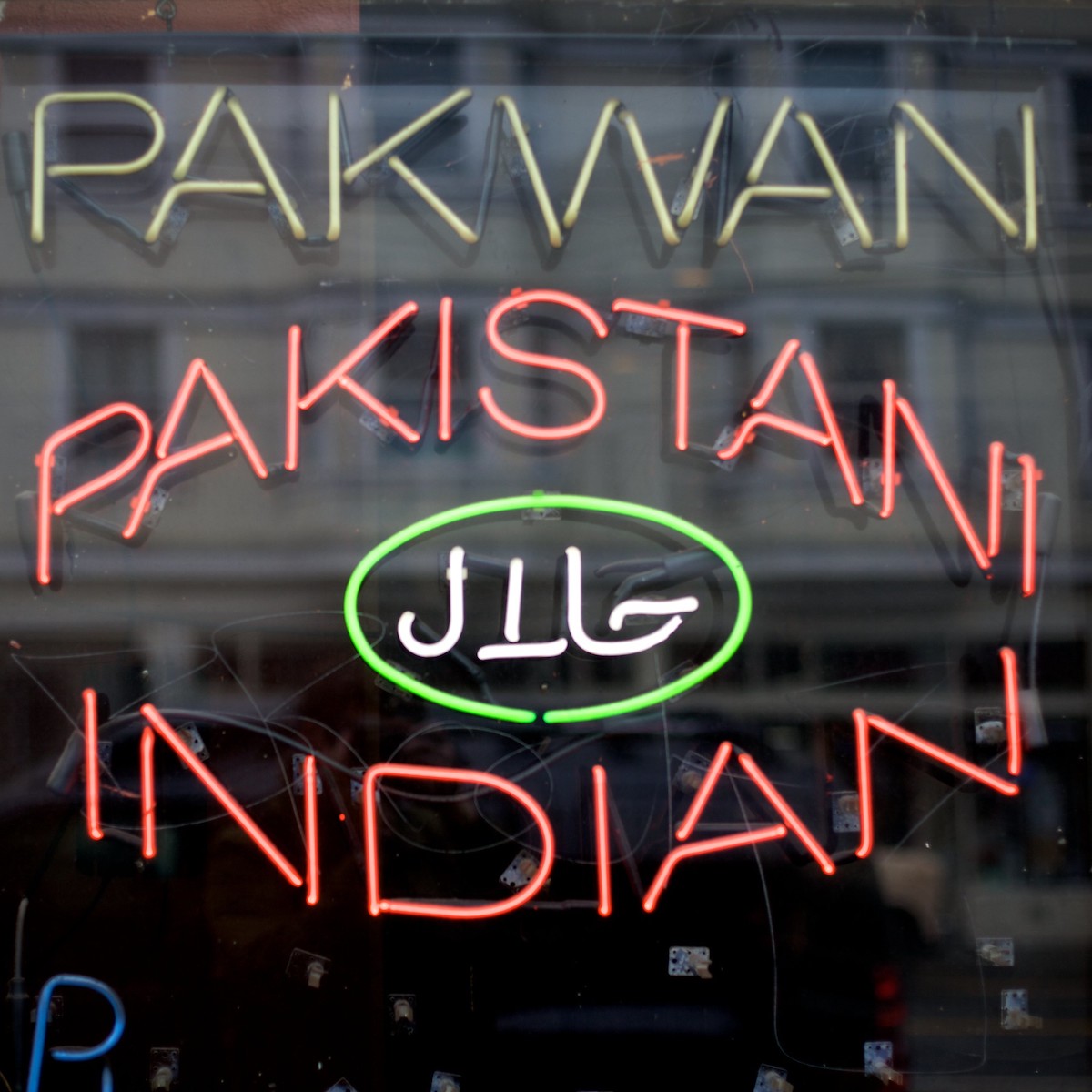 close up of a neon sign in a restaurant window. Yellow letters read "Pakwan" and read letters underneath read "Pakistani Indian"