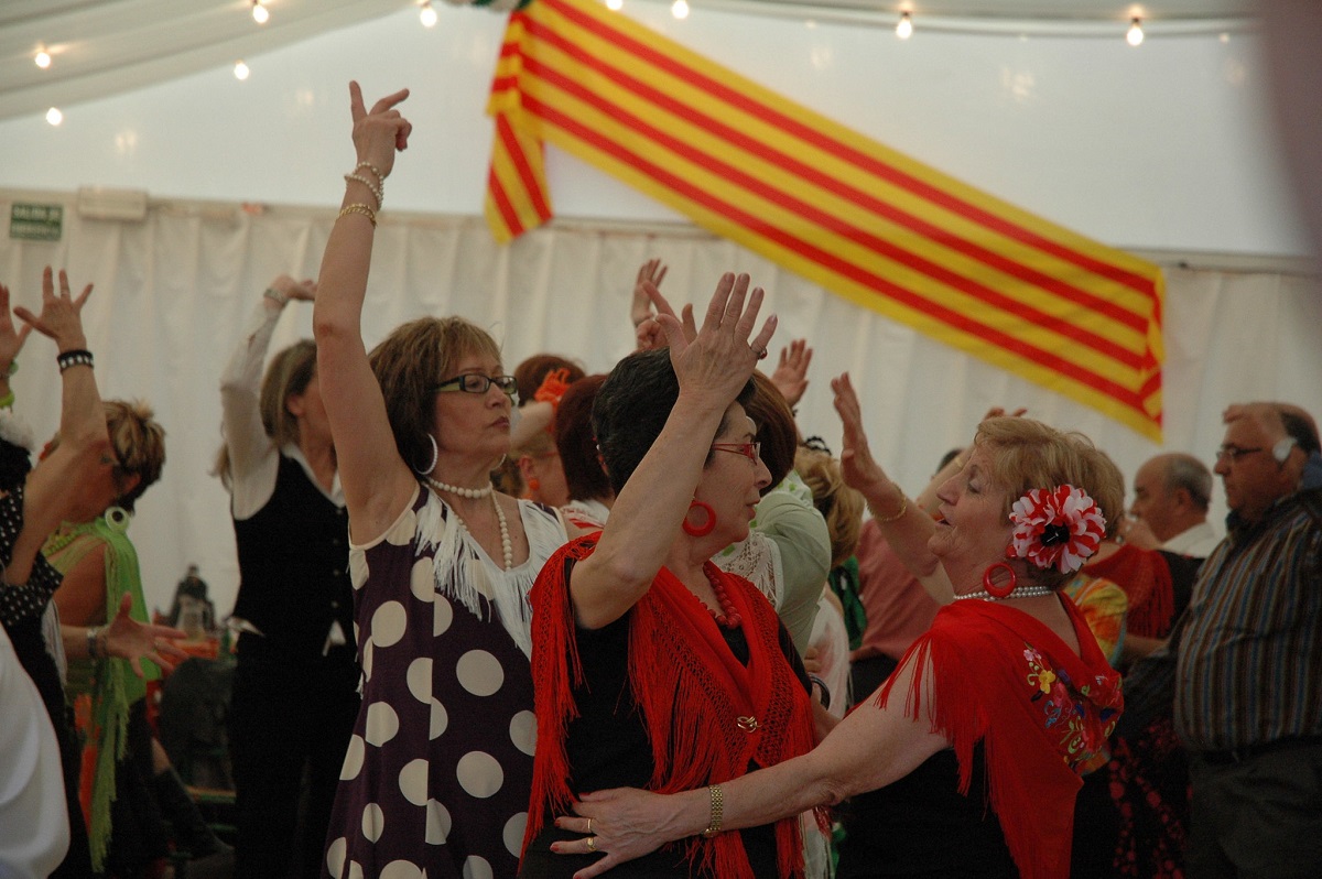 Women dancing in traditional Andalusian feria cosutmes with a Catalan flag in the background