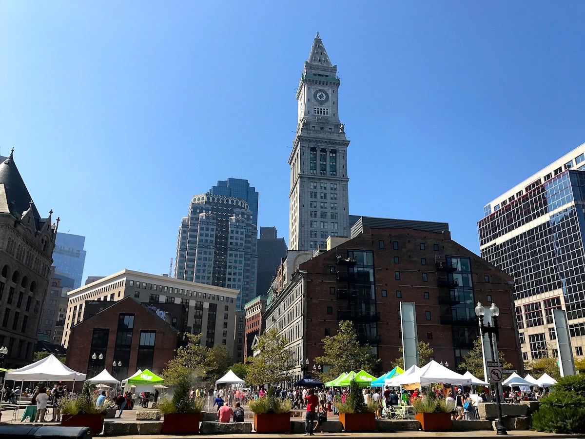 Dozens of tents at the Boston Local Food Festival with tall buildings rising up in the background
