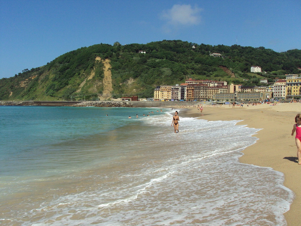 Swimmers on the side of Zurriola Beach in San Sebastian, spain with water, sand, and mountains