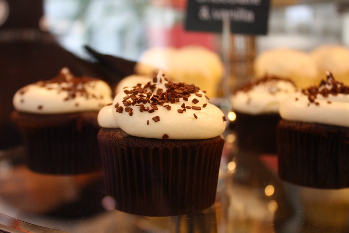 Close up of a platter of chocolate cupcakes with white frosting and dusted with chocolate sprinkles.