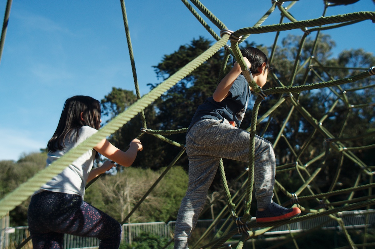 Two children climb on a structure of green ropes at Koret Children's Quarter in Golden Gate Park, a great place for kids to visit in San Francisco