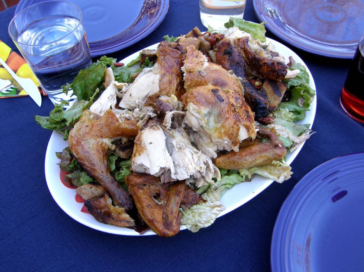 A platter with a whole roasted chicken and warm bread salad on a table set with a blue tablecloth and blue plates