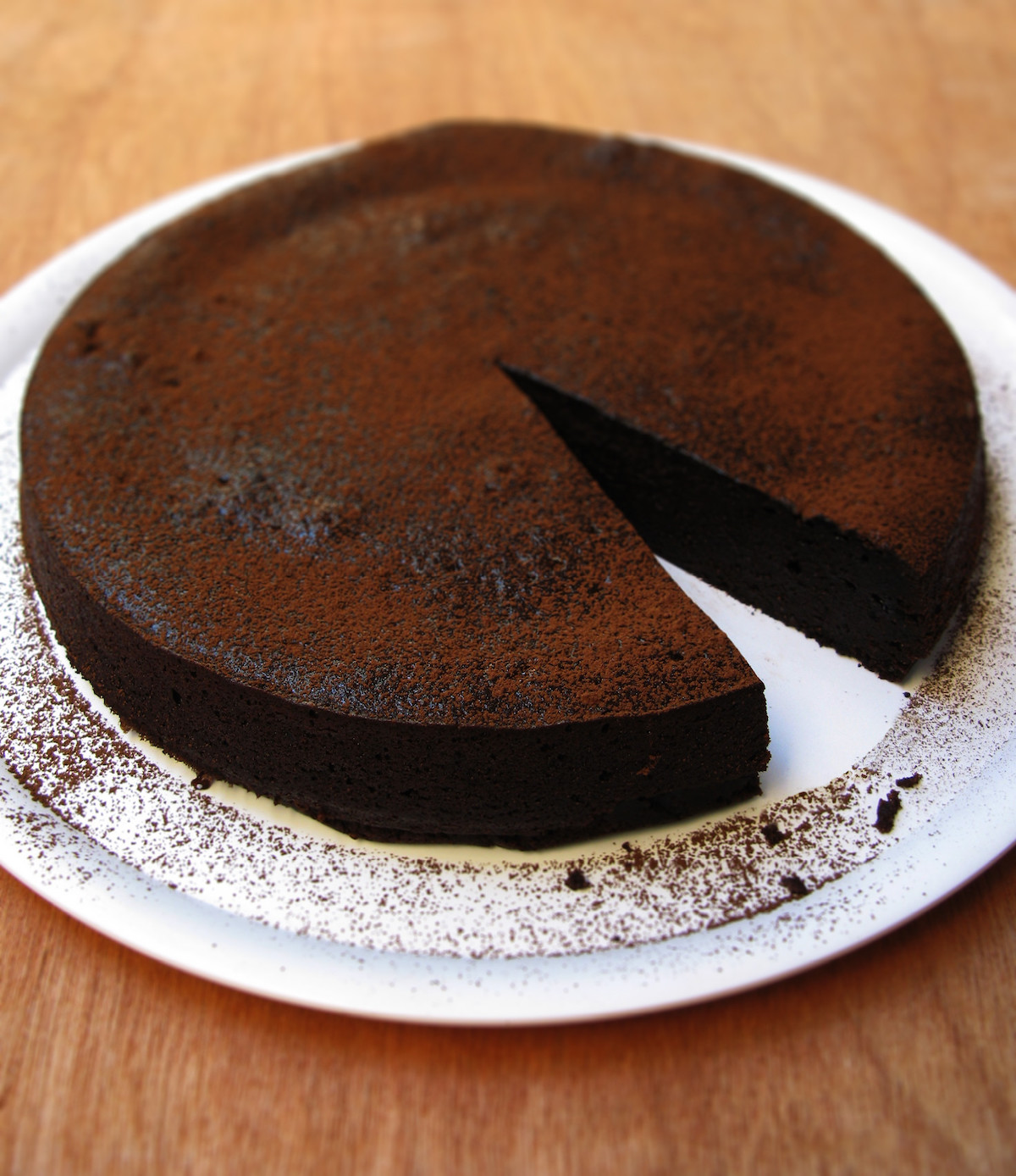 A deeply colored chocolate Caprese cake dusted with cocoa powder sits on a white plate