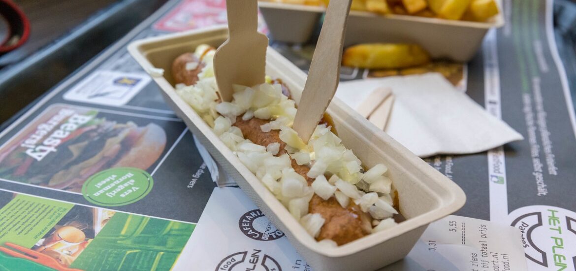 Frikandel, a sausage dish with onion, eaten outside on a table with french fries in Amsterdam