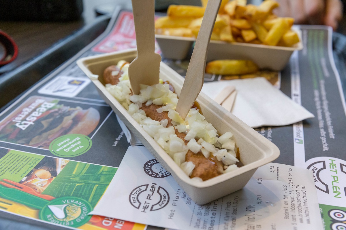 Frikandel, a sausage dish with onion, eaten outside on a table with french fries in Amsterdam
