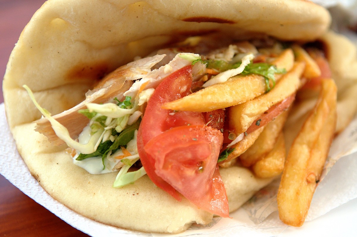 Extreme close up of a Greek gyro, a pita flatbread folded to ensclose pieces of chicken, tomato, greens, and french fies covered in a creamy sauce