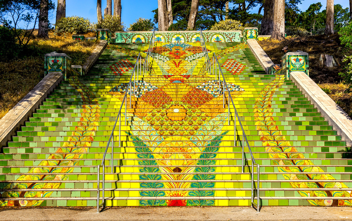 A highly decorated staircase outside in a park. Tiles are painted yellow, green, and red