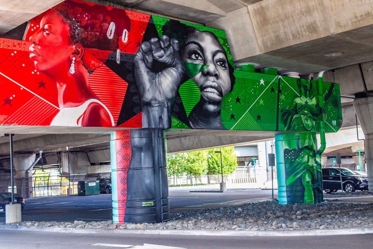 Detailed street art painted underneath an overpass. Bright red and green backgrounds with figures of powerful black women