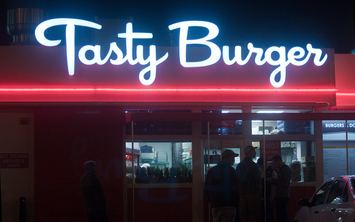 A retry style neon sign reads "Tasty Burger" in white lettering with a red neon stripe underneath encircling the building. Tasty Burger is the ultimate stop for cheap eats in Boston
