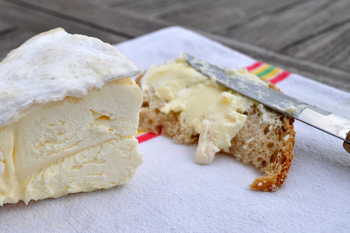 Cut wedge of cheese with smear of cheese on bread with knife on outside eating table