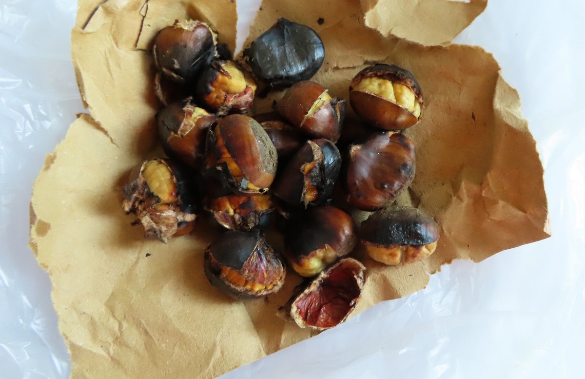 Roasted chestnuts with peeling skin lay on a paper wrapper