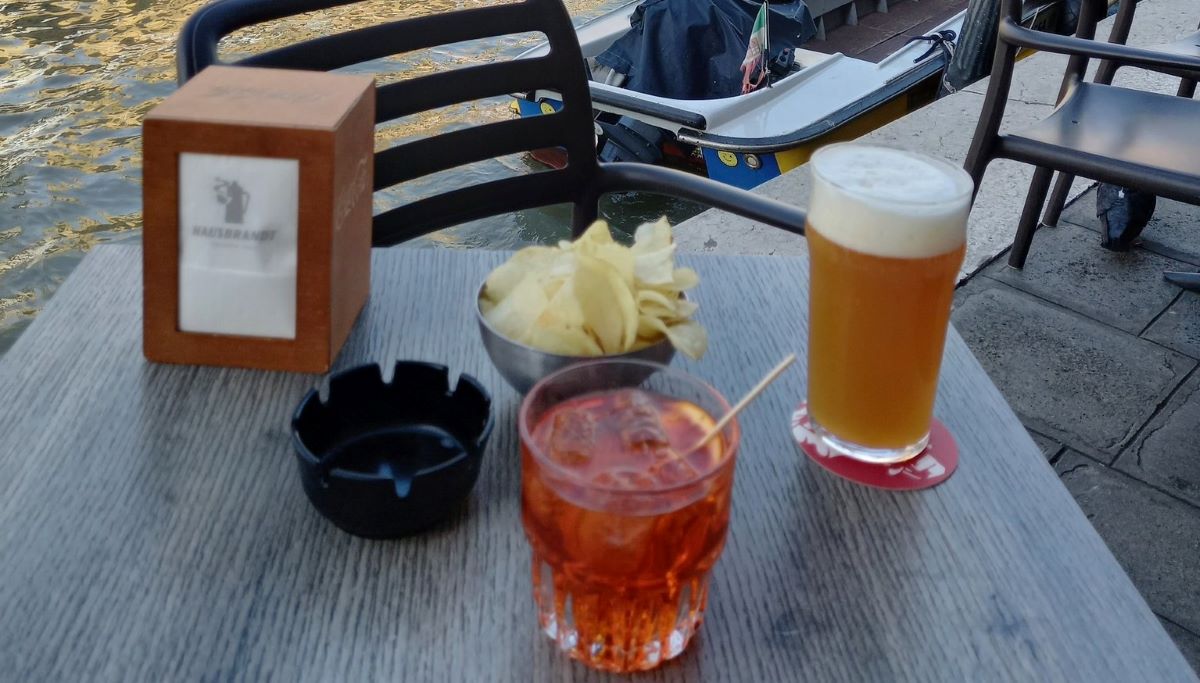 A glass of craft beer in Italy, an Aperol Spritz and a small bowl of chips sitting on a table