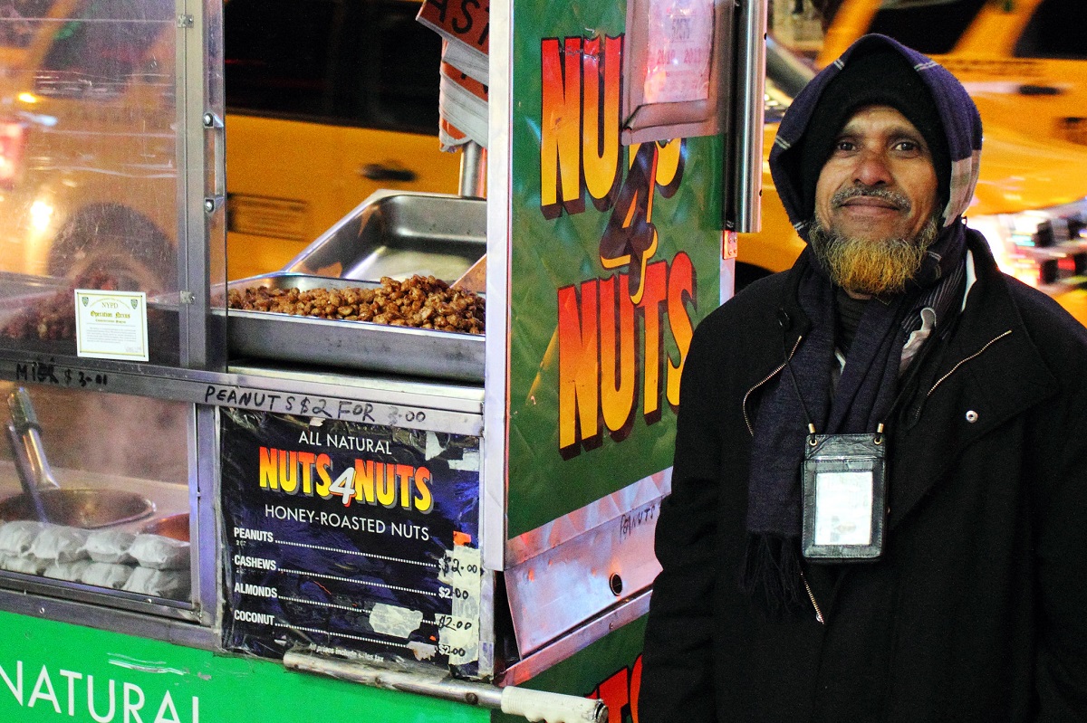 A New York nut vendor smiles while standing beside his food truck