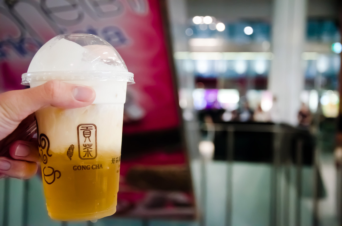 close up of someone holding a plastic cup filled with golden iced tea with the restaurant blurred in the background